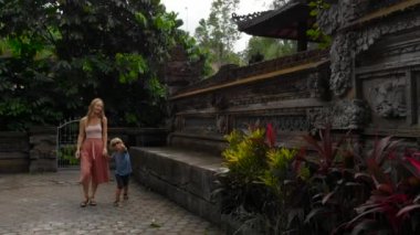 Ağır çekim Genç kadın ve küçük oğlu dolaşan Ubud tapınakta Pura Gunung Lebah üzerinde Bali Adası, Endonezya