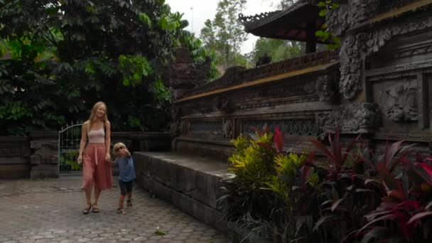 在印度尼西亚巴厘岛乌布的 Pura Gunung Lebah 寺散步的年轻女子和小儿子的慢动作 — 图库视频影像