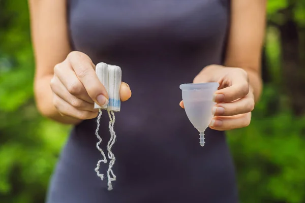 Руки молодої жінки, що тримають різні види засобів жіночої гігієни - менструальна чашка та тампони — стокове фото