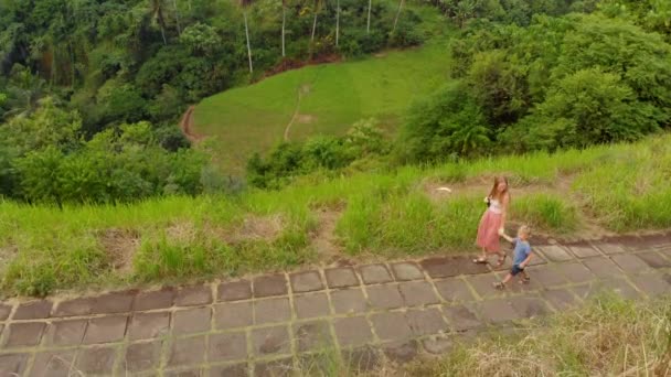 Tiro aéreo de uma jovem mulher e seu filho caminhando na Caminhada de Artistas Caminhada de Cordilheira de Campuhan na aldeia de Ubud na ilha de Bali — Vídeo de Stock