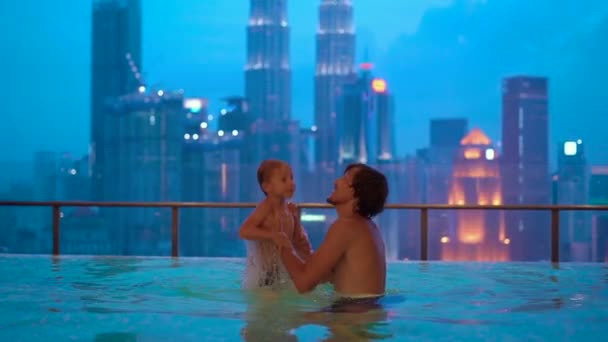 Superslowmotion plan d'un jeune homme et son petit fils s'amusant dans une piscine d'eau sur le toit avec vue sur les gratte-ciel — Video