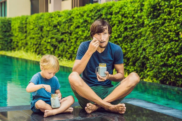 Pai e filho comem sobremesa com sementes de chia e mangas na piscina pela manhã. alimentação saudável, comida vegetariana, dieta e conceito de pessoas — Fotografia de Stock