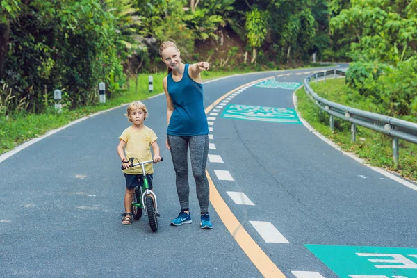 Σπορ γυναίκα τρέχει στο δρόμο με την Ανατολή. Γιος πηγαίνει να ισορροπία ποδήλατο. Έννοια της ευεξίας περιλαμβάνει γυμναστήριο και προπόνηση — Φωτογραφία Αρχείου