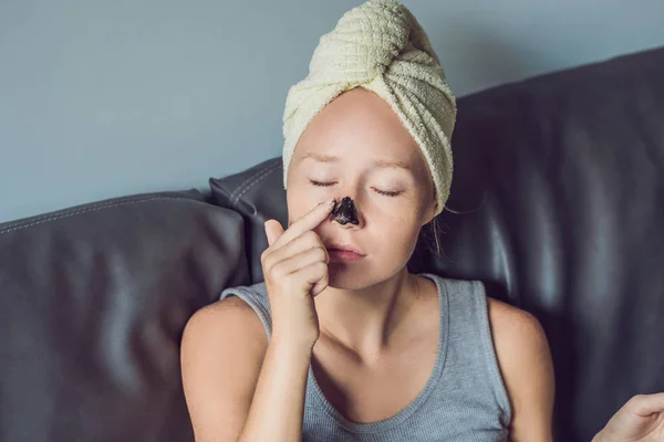 Beautiful young woman relaxing with face mask at home. Happy joyful woman applying black mask on face — Stock Photo, Image
