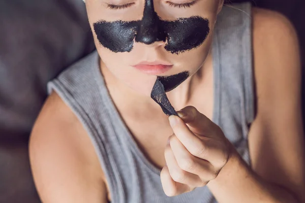 Hermosa mujer joven que se relaja con mascarilla en casa. Feliz mujer alegre aplicando máscara negra en la cara — Foto de Stock