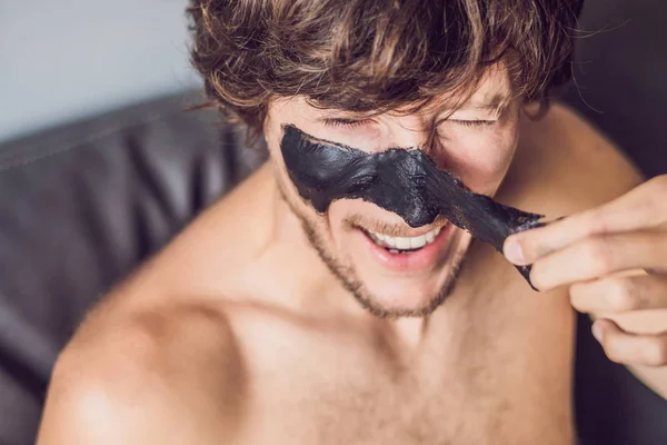 Счастливый человек в черной маске на лице. Фотограф получает спа-процедуры. Концепция ухода за кожей — стоковое фото