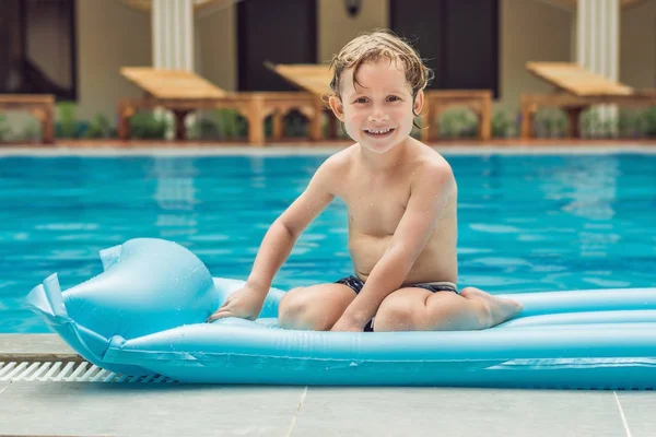 Chico sonriente en el colchón inflable azul en la piscina — Foto de Stock