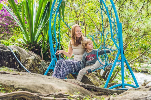 Mãe e filho em um balanço em um parque tropical — Fotografia de Stock