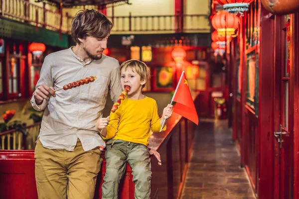 Mutlu baba ve oğul Çin bayrak Çin pazarına arka plan üzerinde geleneksel Çince şekerlenmiş meyve yeme ile.