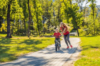 Genç Anne oğlunu parkta Bisiklete binmek kullanmayı öğretmek