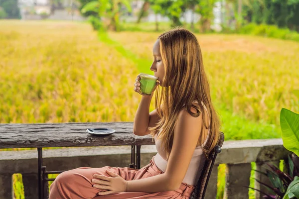 Jovem mulher segurando xícara de matcha Latte, chá verde, na velha mesa de fundo de madeira — Fotografia de Stock