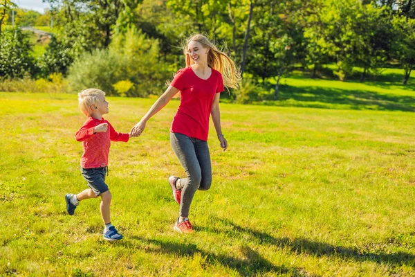 Máma a syn běžet na zelené trávě. Šťastná rodina v parku — Stock fotografie