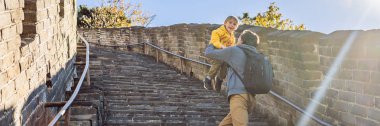 Happy cheerful joyful tourists dad and son at Great Wall of China having fun on travel smiling laughing and dancing during vacation trip in Asia. Chinese destination. Travel with children in China clipart