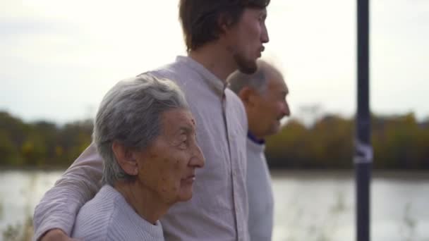 Scatto al rallentatore di un giovane che cammina con i nonni su una passerella lungo un fiume — Video Stock