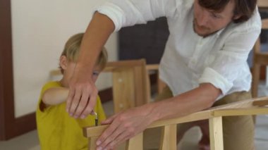 Baba ve oğul ahşap mobilya küçük parçalar bir araya getirin. Küçük çocuk babası bir sandalye bir araya yardımcı olur..
