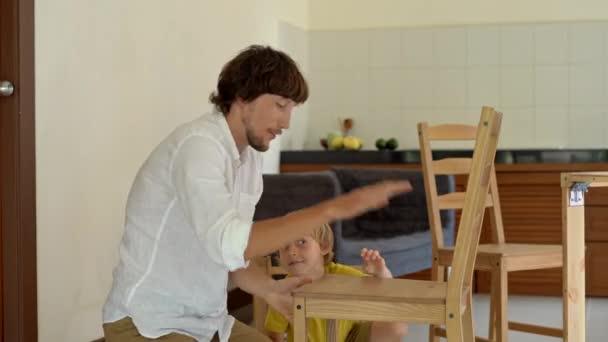 Pai e filho montar móveis de madeira de pequenas peças. Depois de terminar uma cadeira montar homem coloca seu filho em uma cadeira e dá-lhe um cinco . — Vídeo de Stock