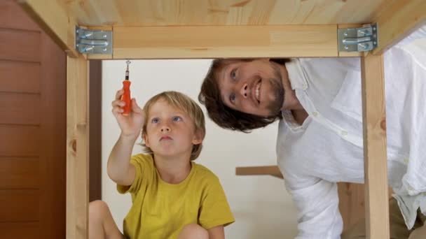 Père et fils assemblent des meubles en bois à partir de petites pièces. Petit garçon aide son père à assembler une table . — Video