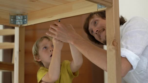 Отец и сын собирают деревянную мебель из мелких деталей. Мальчик помогает отцу собрать стол. . — стоковое видео