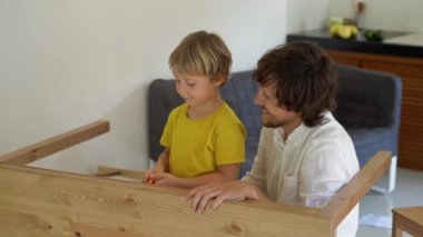 Baba ve oğul ahşap mobilya küçük parçalar bir araya getirin. Küçük çocuk babası bir tablo birleştirmek için yardımcı olur..