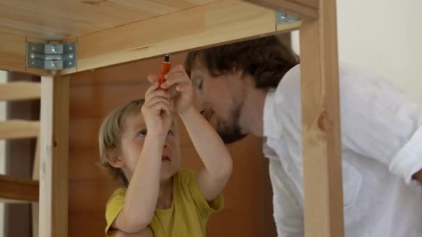 Vader en zoon monteren houten meubilair van kleine onderdelen. Kleine jongen helpt zijn vader te monteren van een tabel. — Stockvideo