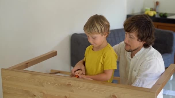 Pai e filho montar móveis de madeira de pequenas peças. Menino ajuda seu pai a montar uma mesa . — Vídeo de Stock
