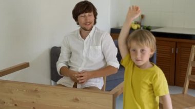 Baba ve oğul ahşap mobilya küçük parçalar bir araya getirin. Küçük çocuk babası bir tablo birleştirmek için yardımcı olur. Adam ve çocuk birbirlerine beş bir tablo bitirdikten sonra araya vermek.