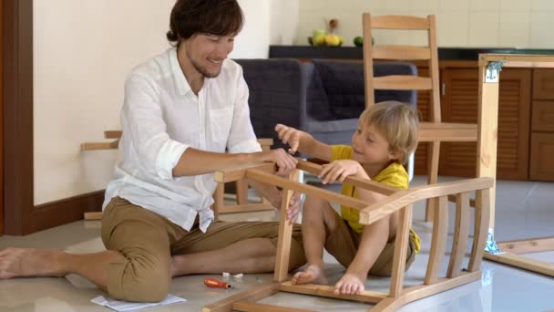 Padre e hijo montan muebles de madera de pequeñas piezas. Pequeño niño ayuda a su padre a montar una silla . — Vídeo de stock