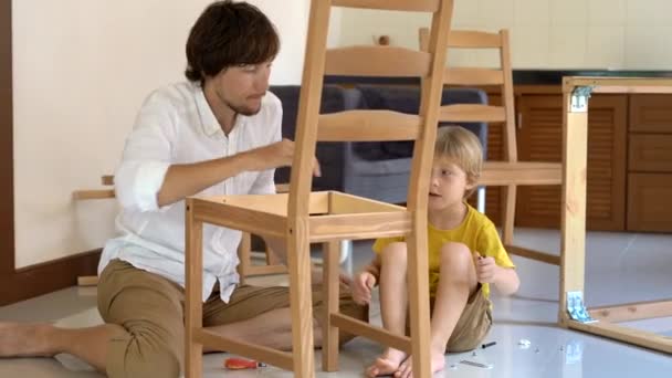 Vater und Sohn montieren Holzmöbel aus Kleinteilen. Kleiner Junge hilft seinem Vater, einen Stuhl zusammenzubauen. — Stockvideo