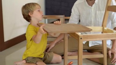 Baba ve oğul ahşap mobilya küçük parçalar bir araya getirin. Küçük çocuk babası bir sandalye bir araya yardımcı olur.