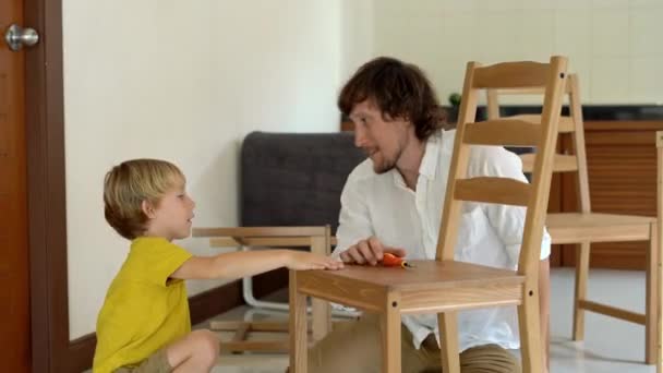 Père et fils assemblent des meubles en bois à partir de petites pièces. L'homme et le garçon se donnent cinq après avoir terminé une chaise assembler . — Video