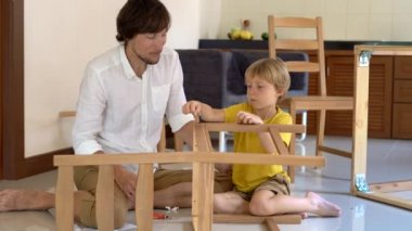 Baba ve oğul ahşap mobilya küçük parçalar bir araya getirin. Küçük çocuk babası bir sandalye bir araya yardımcı olur..