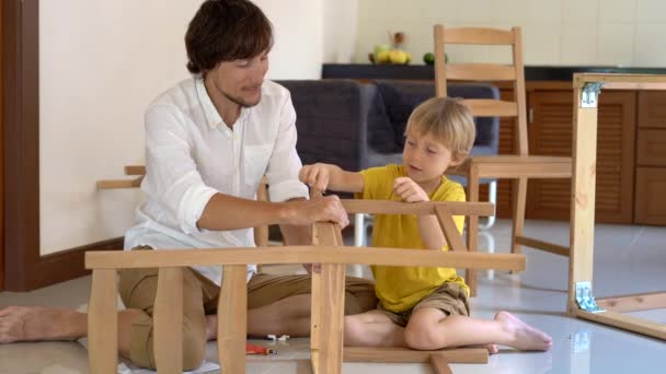 Padre e hijo montan muebles de madera de pequeñas piezas. Pequeño niño ayuda a su padre a montar una silla . — Vídeo de stock