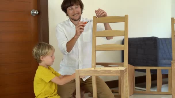 Père et fils assemblent des meubles en bois à partir de petites pièces. Petit garçon aide son père à assembler une chaise . — Video