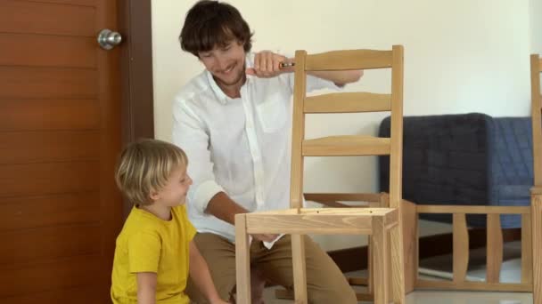 Pai e filho montar móveis de madeira de pequenas peças. Menino ajuda seu pai a montar uma cadeira . — Vídeo de Stock