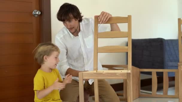 父子双方用小零件组装木制家具。小男孩帮他父亲组装一把椅子. — 图库视频影像