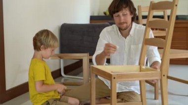Baba ve oğul ahşap mobilya küçük parçalar bir araya getirin. Küçük çocuk babası bir sandalye bir araya yardımcı olur..