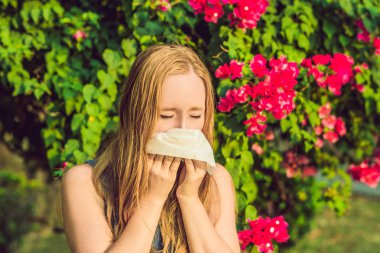 Polen alerji kavramı. Genç kadın hapşırmak için gidiyor. Çiçekli ağaçlar arka planda