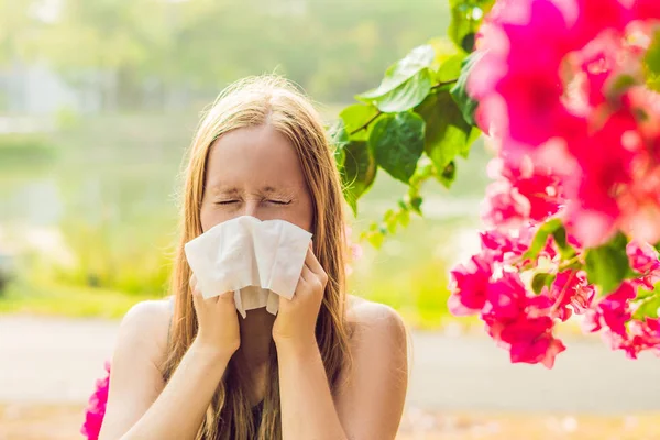 Il concetto di allergia al polline. Una giovane donna starnutira '. Alberi da fiore sullo sfondo — Foto Stock