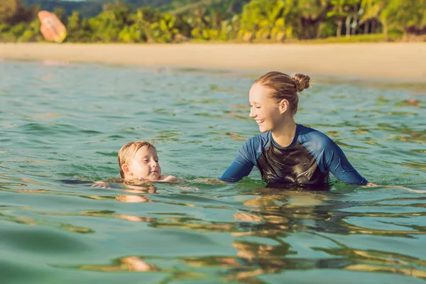 Donna istruttrice di nuoto per bambini sta insegnando a un ragazzo felice a nuotare nel mare — Foto Stock