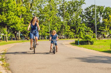 Mutlu aile açık havada bisiklet sürme ve gülümseyerek. Anne bir bisiklet ve bir balancebike oğlu