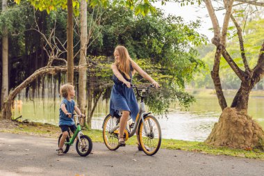 Mutlu aile açık havada bisiklet sürme ve gülümseyerek. Anne bir bisiklet ve bir balancebike oğlu