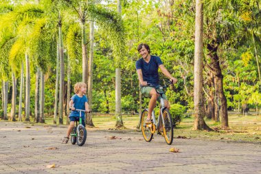 Mutlu aile açık havada bisiklet sürme ve gülümseyerek. Babası bir bisiklet ve bir balancebike oğlu