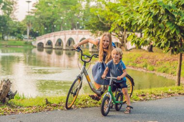 Mutlu aile açık havada bisiklet sürme ve gülümseyerek. Anne bir bisiklet ve bir balancebike oğlu