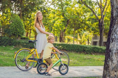 Mutlu aile açık havada bisiklet sürme ve gülümseyerek. Anne bir bisiklet ve bir balancebike oğlu