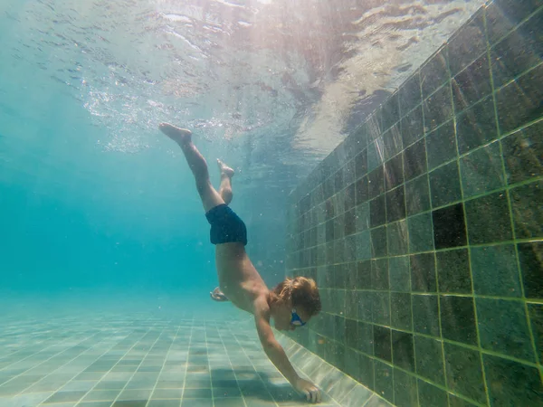 Um menino está nadando debaixo d 'água em uma piscina, sorrindo e segurando a respiração, com óculos de natação — Fotografia de Stock