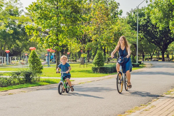 Happy family is riding bikes outdoors and smiling. Mom on a bike and son on a balancebike