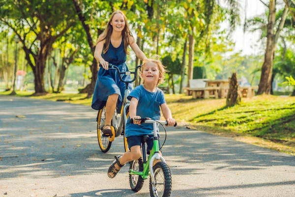 Happy family is riding bikes outdoors and smiling. Mom on a bike and son on a balancebike