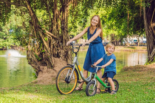 Happy family is riding bikes outdoors and smiling. Mom on a bike and son on a balancebike