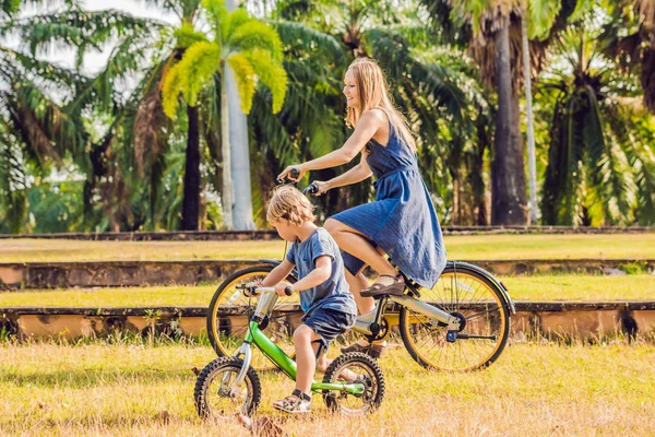 Happy family is riding bikes outdoors and smiling. Mom on a bike and son on a balancebike