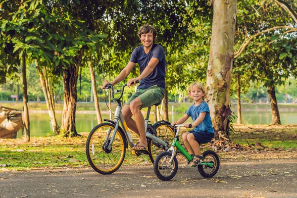 Happy family is riding bikes outdoors and smiling. Father on a bike and son on a balancebike